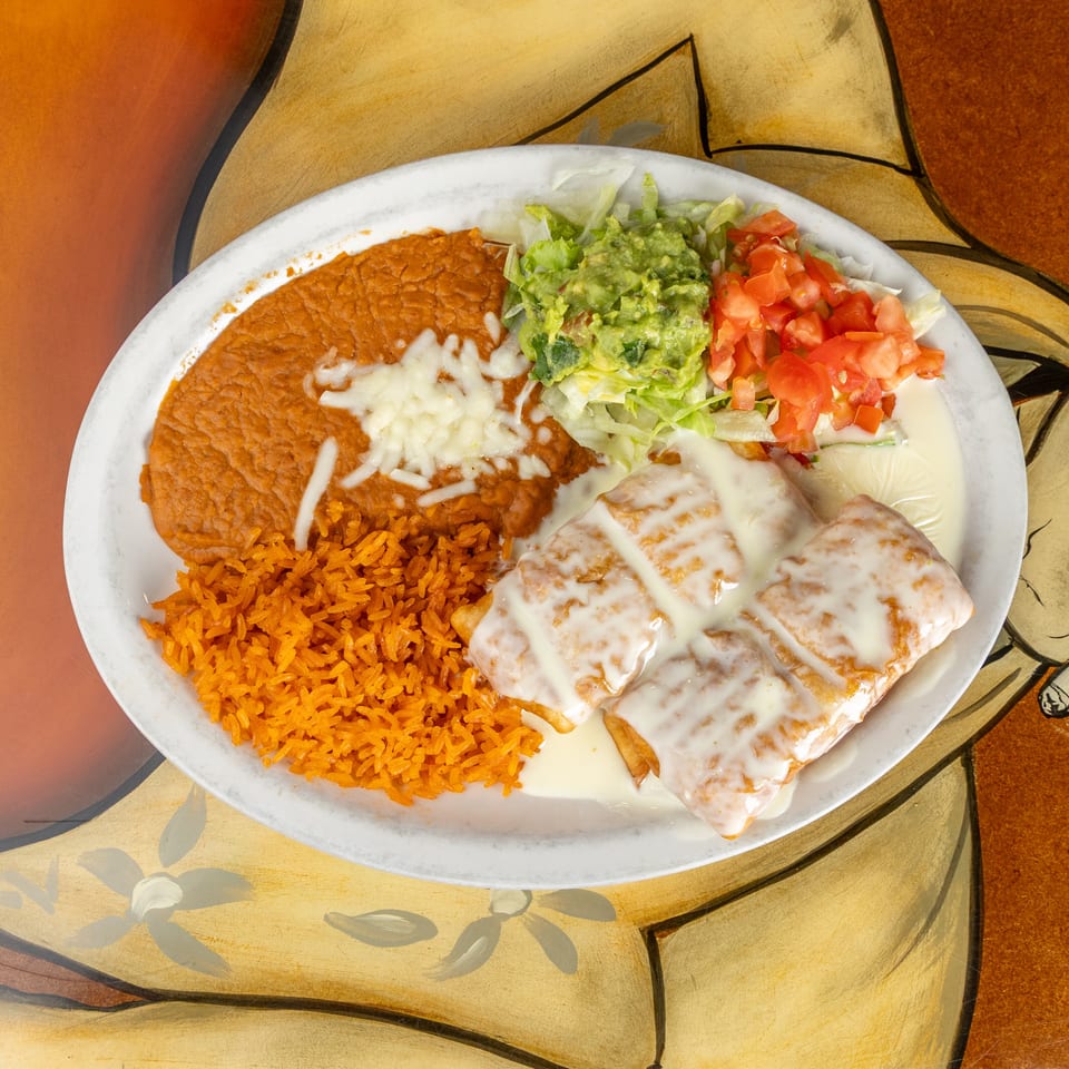 Mexican platter with rice, refried beans, cheesy enchiladas, guacamole, lettuce, diced tomatoes, and cream sauce.