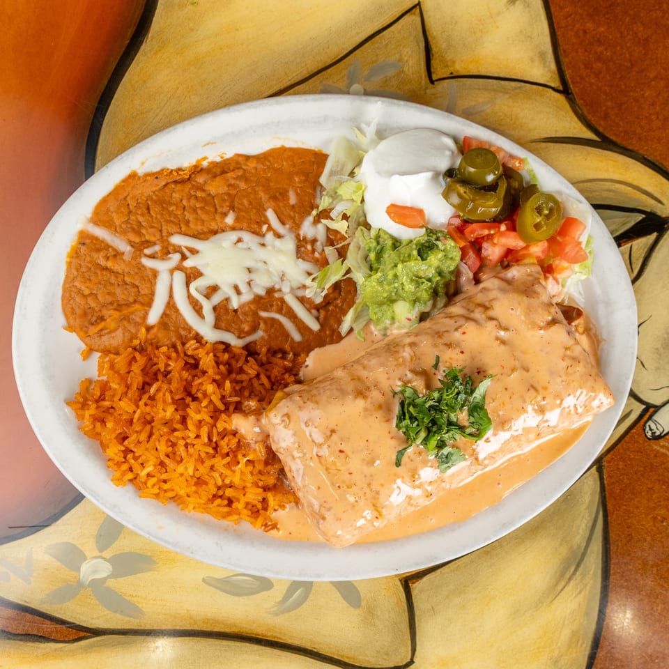 Mexican-style platter with rice, refried beans, creamy enchiladas, guacamole, sour cream, tomatoes, lettuce, and jalapeños.