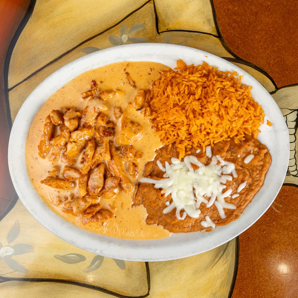 Plate of creamy chicken, orange rice, and cheese-topped refried beans on a colorful restaurant table.